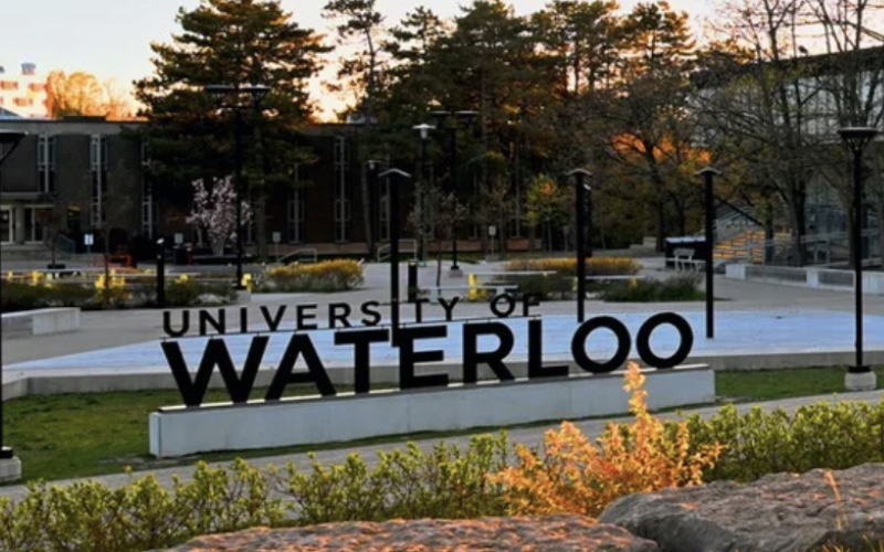 Foto von Aufstellbuchstaben auf einem Betonsockel, die den Schriftzug "University of Waterloo" zeigen. Im Vordergrund eine Hecke und im Hintergrund Bäume bei Abendstimmung. So erwartet die Uni unsere Wissenschaftler für die Energiewende.